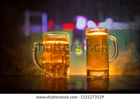 Creative concept. Beer glasses on table at dark toned foggy background with blurred view of playing game at the stadium. Selective focus