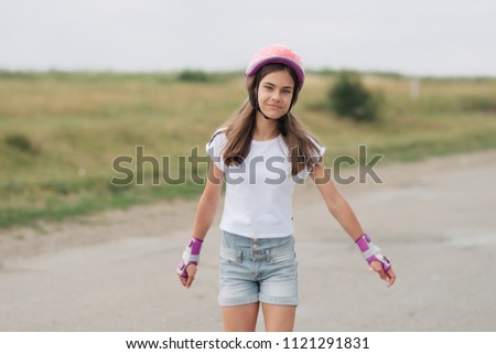 Smiling girl on pink roller skates riding outdoors on the street. Young girl wearing pink helmet and knee pads. Summer entertainment.