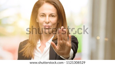 Middle age woman wearing jacket annoyed with bad attitude making stop sign with hand, saying no, expressing security, defense or restriction, maybe pushing