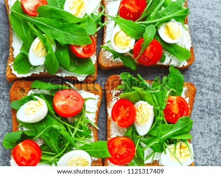 Wheat rye toasts with arugula, quail eggs and cherry tomatoes. The concept of a useful snack. Snack to take along.  Bright tasty and healthy fitness toasts. Open sandwich with arugula and cream cheese