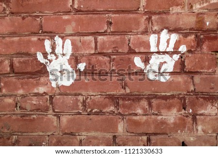 White prints of the palms of the hands on the brick wall