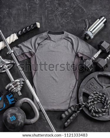 Grey t-shirt and sports equipment on a black background. Top view. Motivation. Copy space