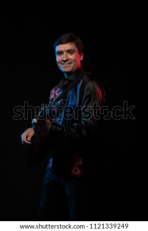 Artist musician A brunette man in a folk shirt playing a balalaika in scenic blue and red light on a black stage