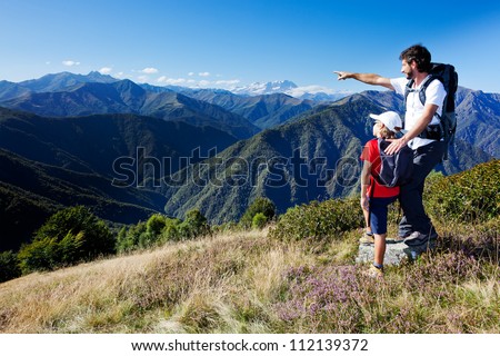 Man and young boy standing in a mountain meadow. The man points to a direction, showing something to the boy. Summer season, clear blue sky. Monte Rosa Massif, Piemonte, west italian Alps. Royalty-Free Stock Photo #112139372