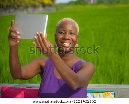 young attractive and happy black african american woman outdoors taking selfie with digital tablet pad on green grass field background enjoying Summer holidays travel at tropical destination