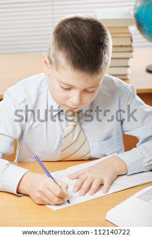 Boy in blue shirt writing while sitting at desk