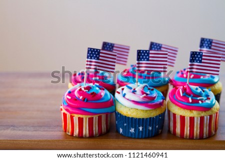 Happy 4th of July conceptual image with patriotic multicolored icing cupcakes and American flags.