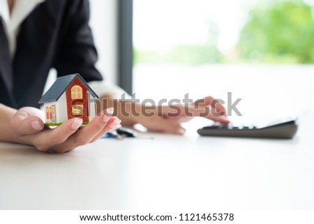 Businesswoman calculating budget before signing real estate project contract with house model at the table in the office