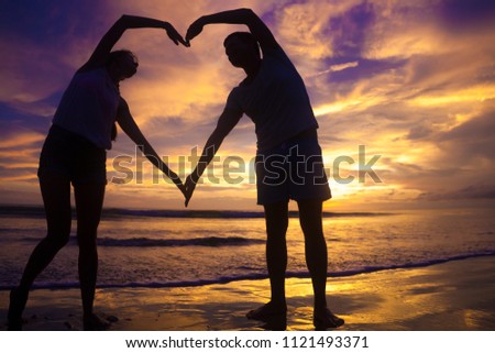 sunset silhouette of young couple in love holding hands at beach