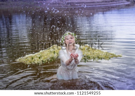 Nice blonde girl with white flower wings in a water of a river