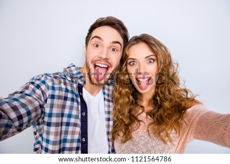 Self portrait of crazy funky couple gesturing tongue out having online meeting shooting selfie on front camera isolated on grey background