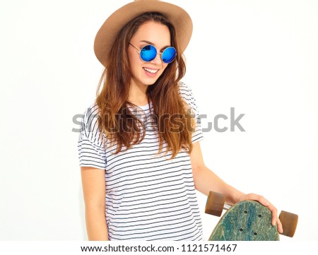 Portrait of young stylish girl model in casual summer clothes in brown hat posing with longboard desk. Isolated on white