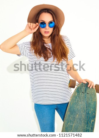 Portrait of young stylish girl model in casual summer clothes in brown hat posing with longboard desk. Isolated on white