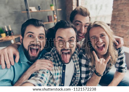Self portrait of four attractive comic crazy funny foolish guys with hairstyle, showing tongue out and rock and roll symbol, making selfie on smart phone, front camera, sitting on couch in livingroom