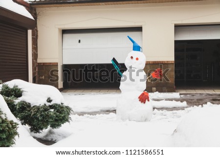 Snowman motorist stands in front of the garage. For decoration use a watering can, a brush and working gloves
