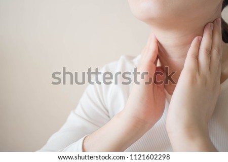Female checking thyroid gland by herself. Close up of woman in white t- shirt touching neck. Thyroid disorder includes goiter, hyperthyroid, hypothyroid, tumor or cancer. Health care. Copy space. Royalty-Free Stock Photo #1121602298