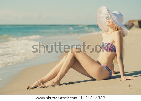 Young woman in bikini and hat relaxing on the beach. Toned in vanilla colors