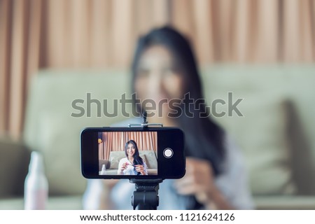 Young Asian cute artist woman beauty vlogger or blogger doing a cosmetic makeup tutorial vlog with brushes looking camera smartphone,recording viral clip share on social media live streaming Internet Royalty-Free Stock Photo #1121624126