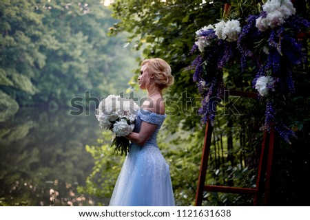 The bride stands at the arch, decorated with flowers, with a large bouquet of white peonies.On-site registration in the Park Wedding walk and photo shoot
