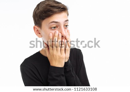 Photo emotional teenager, guy in black t-shirt, shows the emotions of fear, closing his mouth with his hands, on a white background,