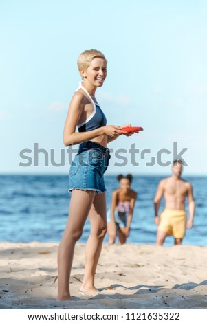 selective focus of interracial friends playing with flying disk on sandy beach