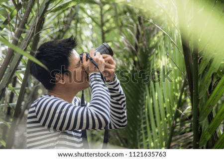 Man traveler hand holding camera  to take a photo in the forest