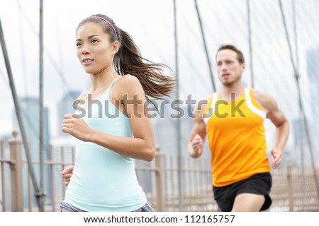 Running couple. Woman and man runner athletes training outside for marathon. Photo from Brooklyn Bridge, New York City, USA. Asian woman and Caucasian man fitness sport models.