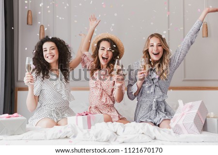 Luxury bachelorette party in posh apartment while happy young three women 20s having fun and drinking champagne under falling confetti Royalty-Free Stock Photo #1121670170