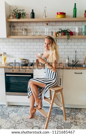 Photo of beautiful woman in long striped dress in kitchen