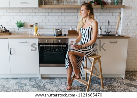 Photo of beautiful woman in long striped dress in kitchen