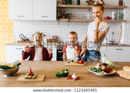 Photo of young mother with daughter and son cutting vegetables at table