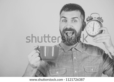 Man drink morning coffee or tea with alarm clock. Happy guy with mulled wine, clock on pink background. Refreshment break and energy.
