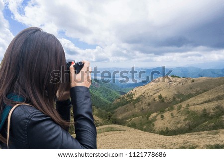 Caucasian female photographer taking photo of mountain and lake landscape