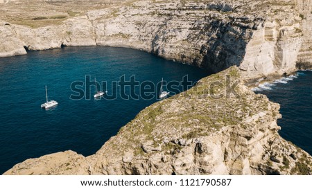 Scenic aerial view of three white yacht sailing boats in the bay of deep blue mediterranean sea with rocky cliffs and island in Gozo, Malta. Shot from above. Travel concept
