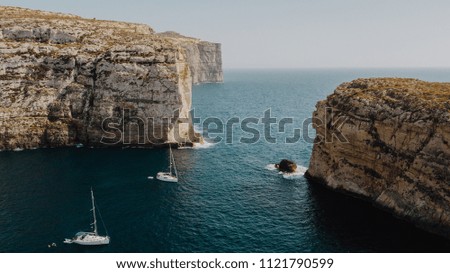 Scenic aerial view of two white yacht sailing boats in the bay of deep blue mediterranean sea with rocky cliffs and precipice in Gozo Island, Malta. Shot from above. Travel concept