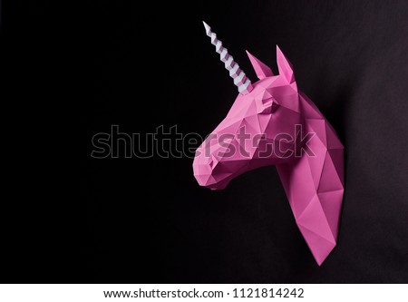 Bright fancy pink origami unicorn's head. Hanging on saturated black wall. Dull colored. Dark background. Innovative interior design details. Straight lines. Original geometrical shape. Royalty-Free Stock Photo #1121814242