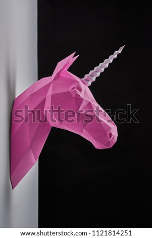 Pink saturated geometrical unicorn's head hanging on grey wall. Black background. Innovative interior design details. Straight lines. Original geometrical shape. Shadows. Decorations shooting.