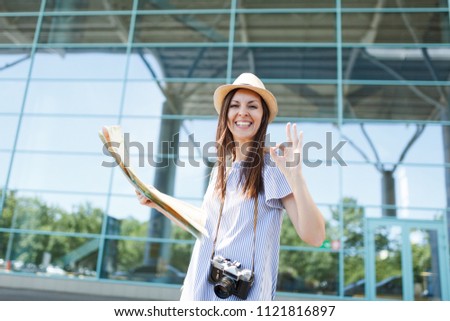 Young joyful traveler tourist woman with retro vintage photo camera hold paper map, show OK gesture at international airport. Female passenger traveling abroad on weekends getaway. Air flight concept