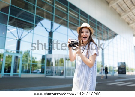 Young surprised joyful traveler tourist woman in hat holding retro vintage photo camera at international airport. Female passenger traveling abroad to travel on weekends getaway. Air flight concept