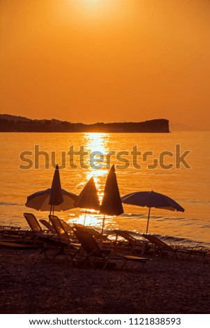 Beach umbrellas and sunbeds on the sea beach at sunset lit by orange backlit