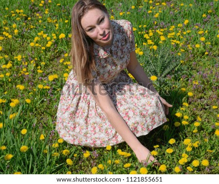 A girl in a dress in a clearing with dandelions. The girl among the flowers.