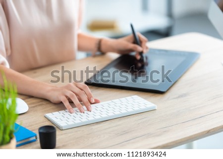 cropped image of female freelancer drawing on graphic tablet at table with computer in home office 