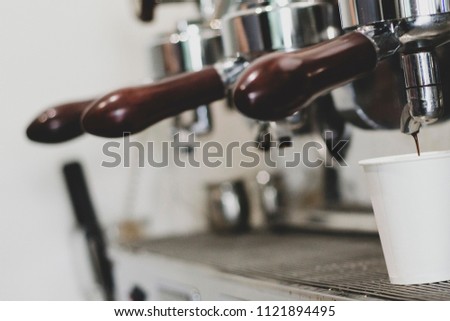 chrome-plated coffee machine parts that brew coffee from a holder in a white paper cup
