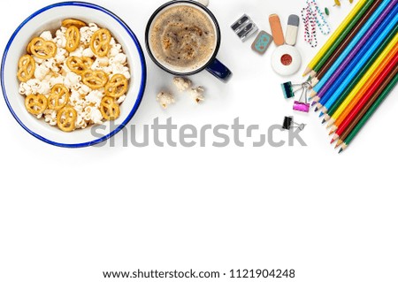 Cup of coffee with snacks and school stationery materials such as crayons, markers, clips, puncher, magnifying glass, erasers on white office table desk. Top view, flat lay with copy space