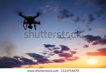 Drone is flying over the field at sunrise. Modern technological background - silhouette of flying machine in glowing red sunset sky.