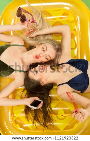 Cute girls in swimsuit posing at studio. Summer portrait caucasian teenagers on a matress background. Concept of summer, summertime, recreation, break, vacation, travel.