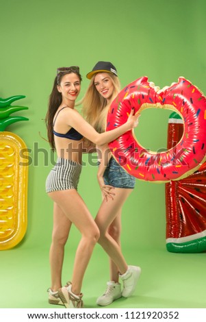 Cute girls in swimsuit posing at studio with inflatable swimming circle. Summer portrait caucasian teenagers on a green background. Concept of summer, summertime, recreation, break, vacation, travel.