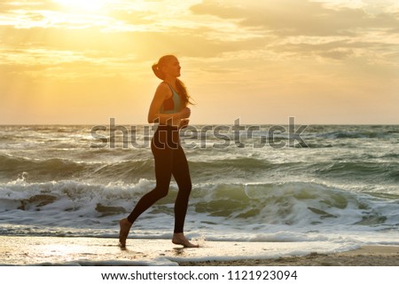 Girl in sportswear running along the surf line. Early morning.