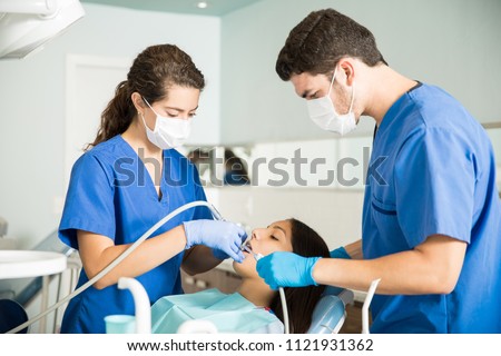 Medical coworkers treating teenage patient with dental equipment at clinic Royalty-Free Stock Photo #1121931362