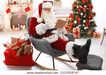 Authentic Santa Claus with glass of milk reading book indoors